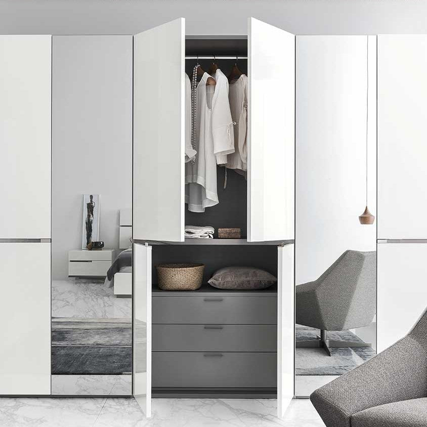 A modern white wardrobe with open doors revealing hanging white clothes and gray drawers underneath. — Castle Furniture